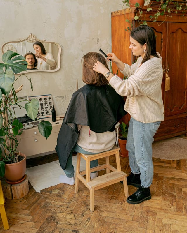 Mira Klausner schneidet im hellen Salon einem Kunden die Haare, im Hintergrund Spiegel und Pflanzen