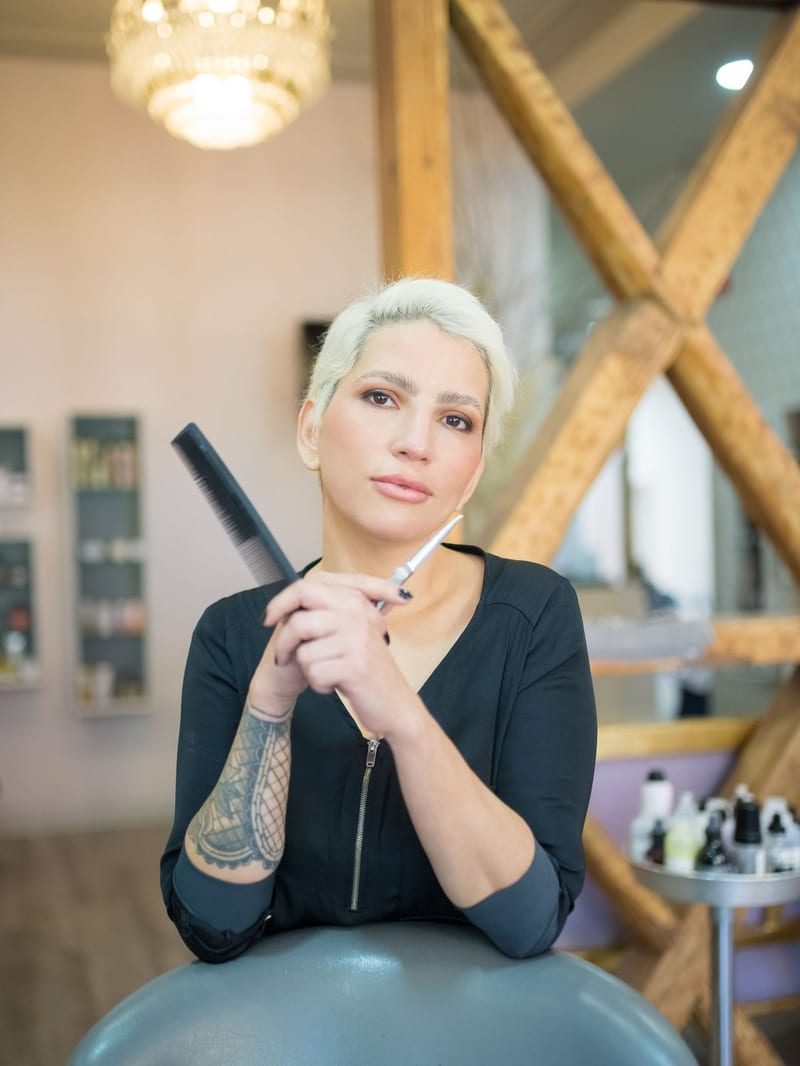Sabine Bäuml lehnt mit Kamm in der Hand an einem Friseurstuhl im hellen Atelier